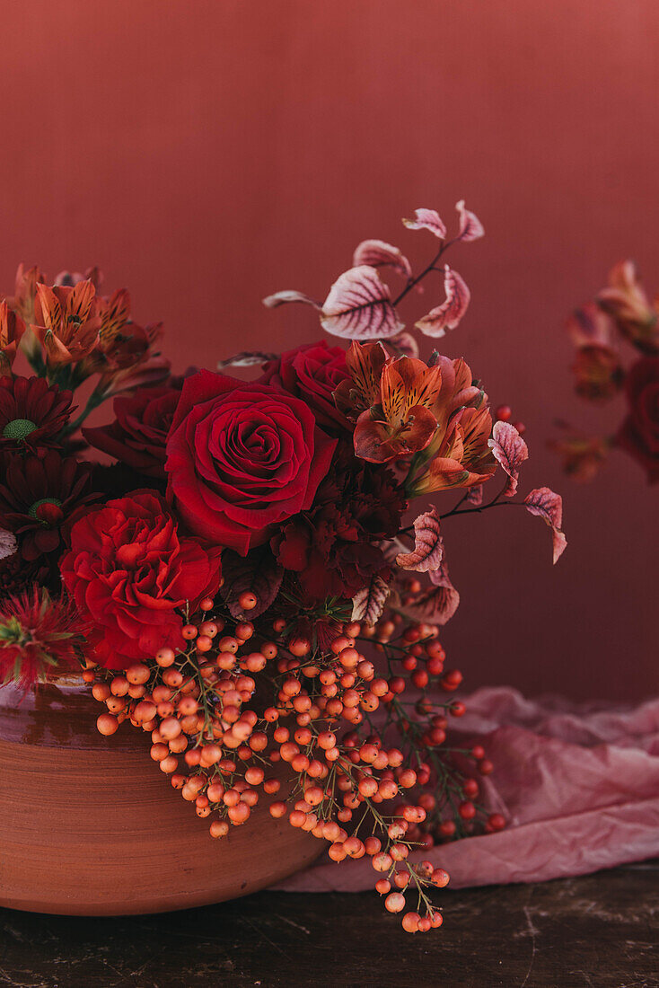 Ausschnitt eines eleganten Blumenstraußes aus frischen, üppigen roten Rosen und Lilien mit Zweigen roter Beeren, die in der Nähe des Stoffes platziert sind