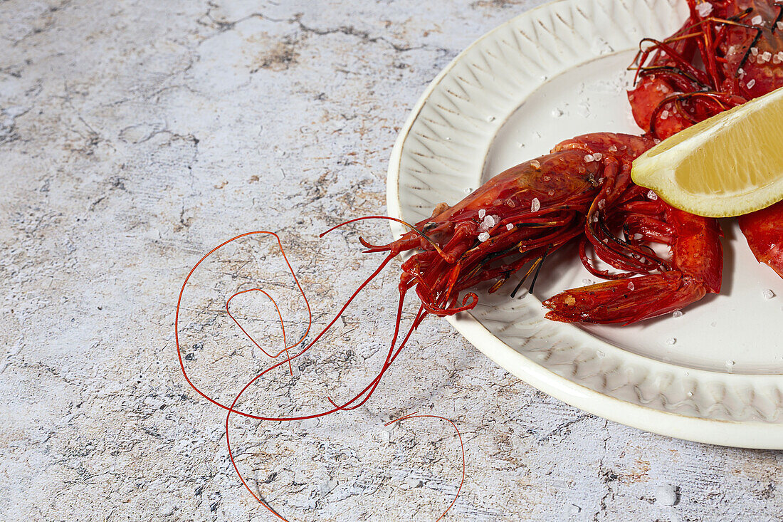 Tasty seafood of cooked red shrimps with fresh lemon slices and coarse salt on white background