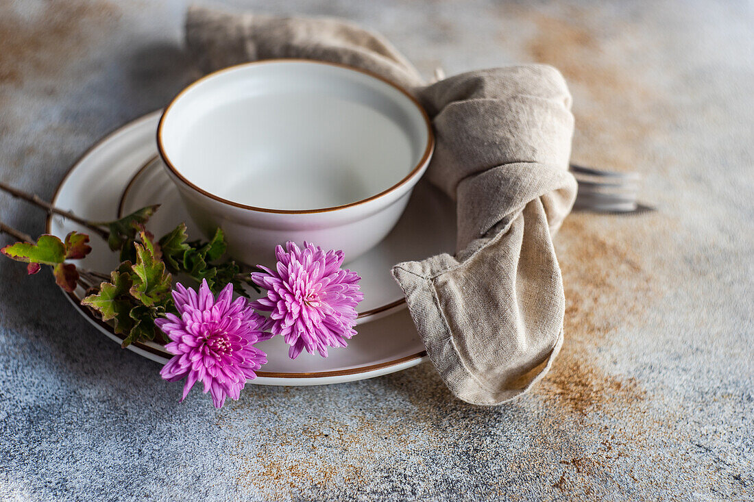 Gedeck mit lila Chrysanthemenblüten auf Betontisch mit Tellern