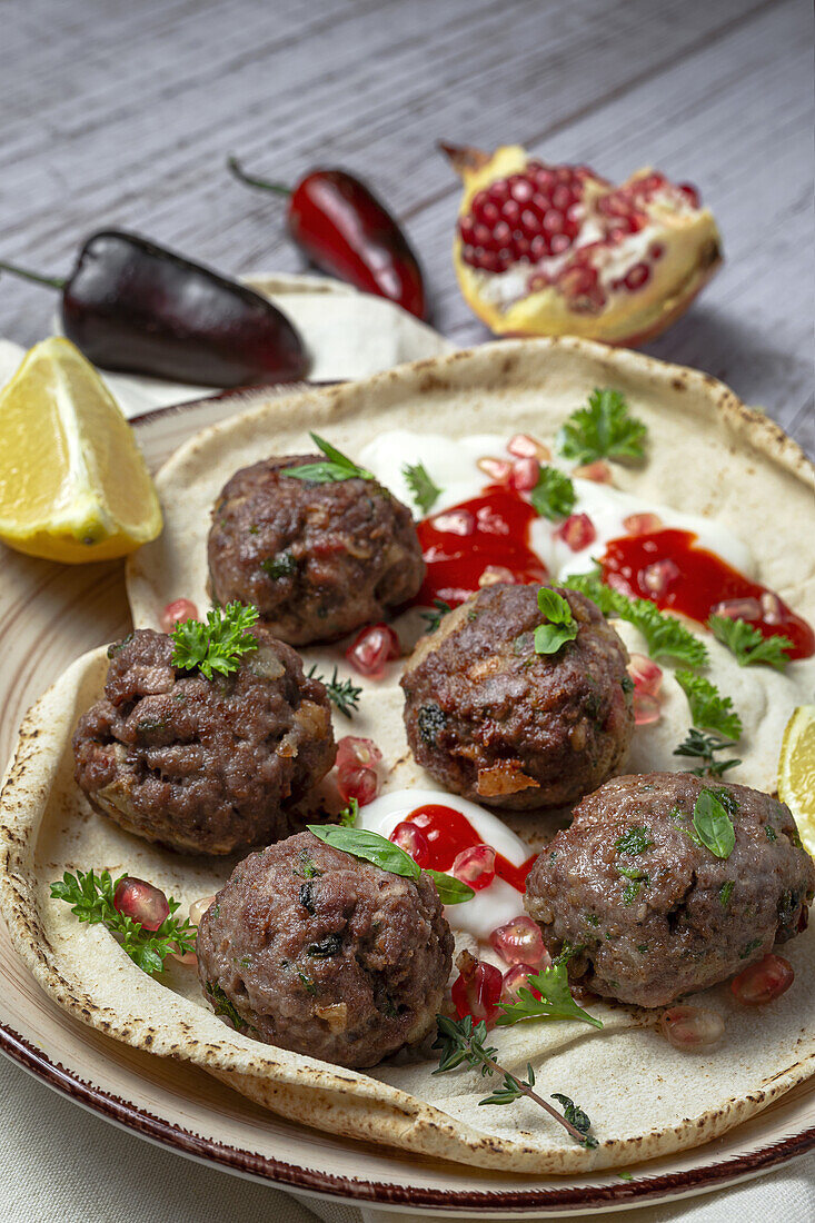 Traditional homemade beef and lamb meatballs with arabic bread, tomato sauce, pomegranate and aromatic herbs. Halal food