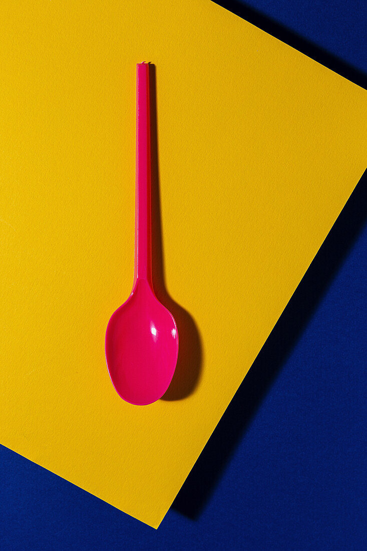 Overhead view of pink eco friendly spoon near yellow and blue carton sheet background