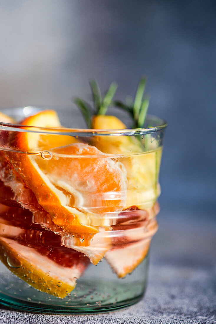 Summer tropical cocktail of vodka and sprite with ripe fruits and rosemary on grey background