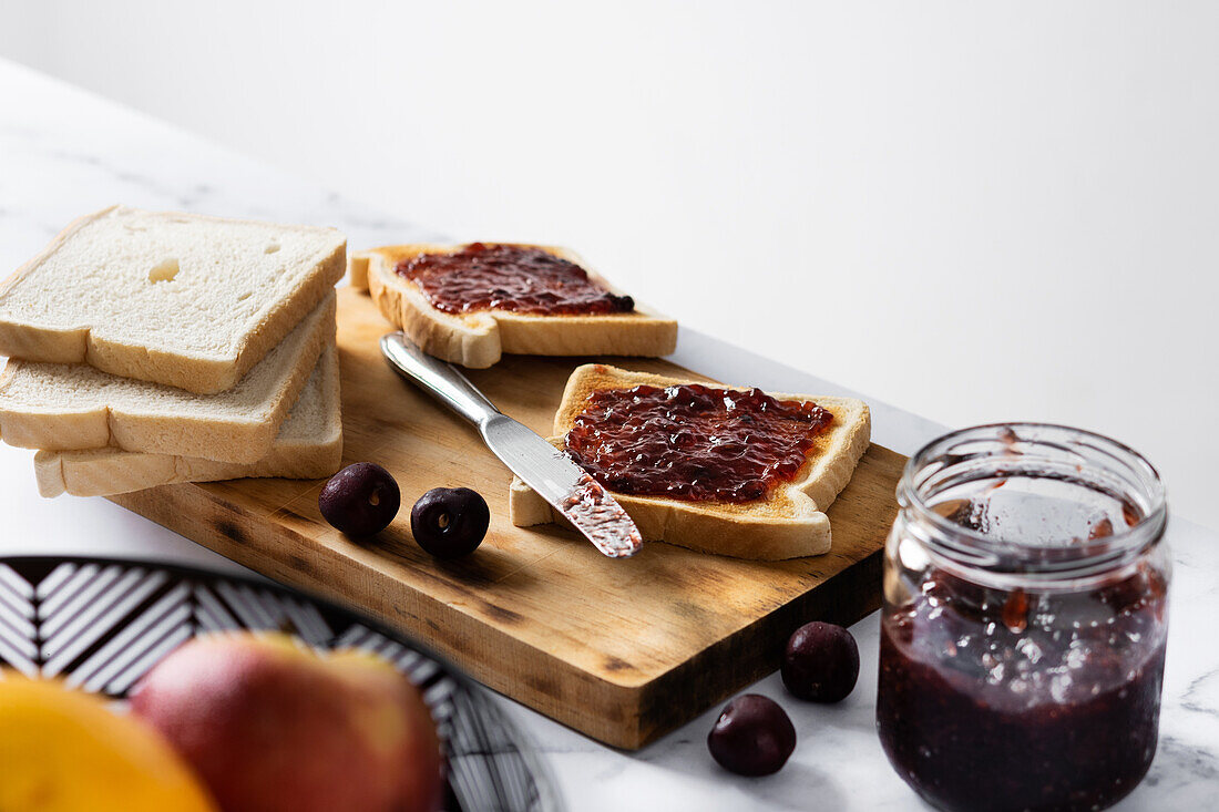 High angle of appetizing crispy toasts with cherry jam served on wooden chopping board near fresh ripe cherries on table