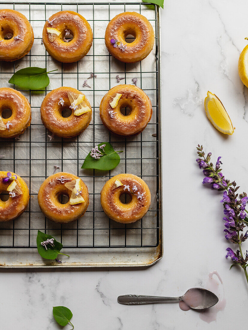 Draufsicht auf leckere Donuts auf Kühlregal mit Blättern zwischen blühenden Lavendelzweigen auf Marmoroberfläche