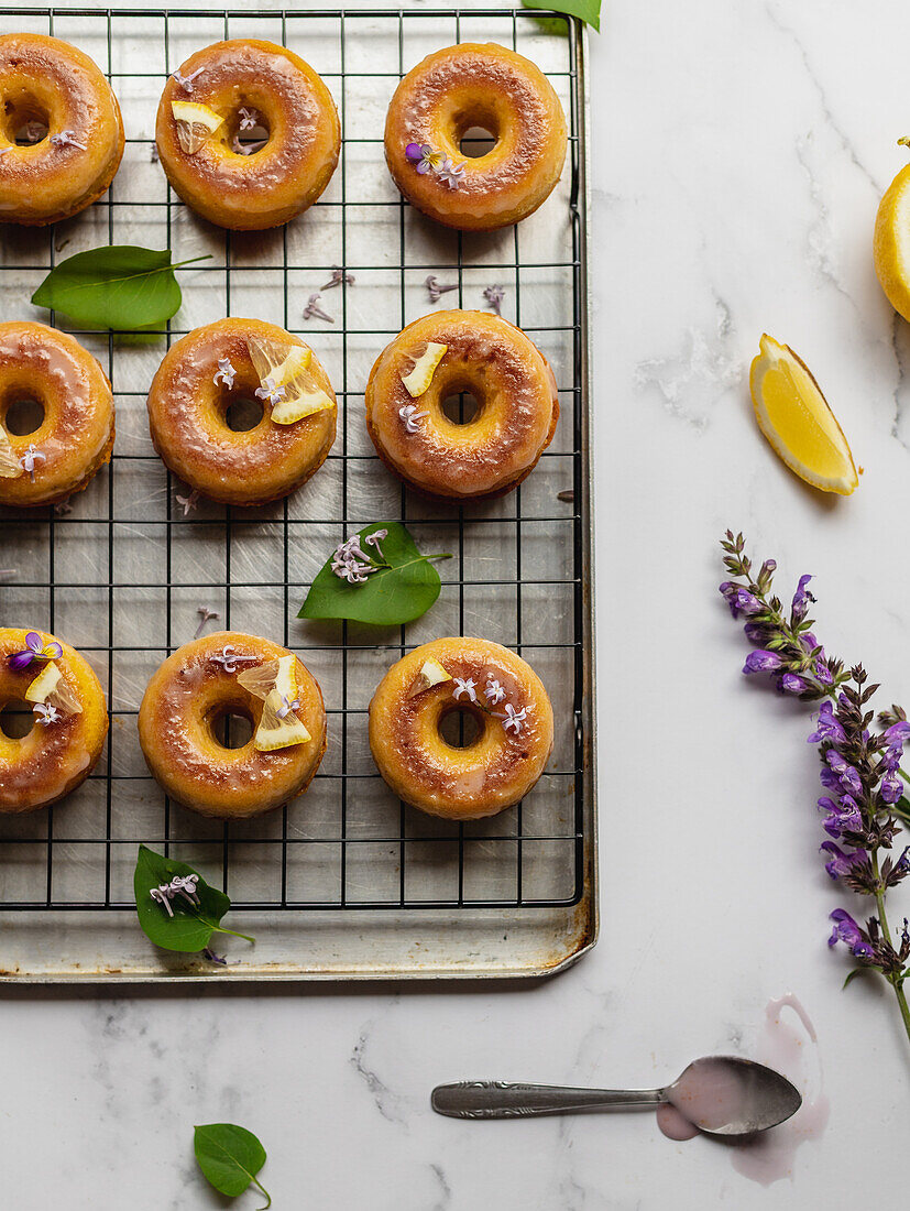 Top view of tasty donuts on cooling rack with leaves between blooming lavender sprigs on marble surface