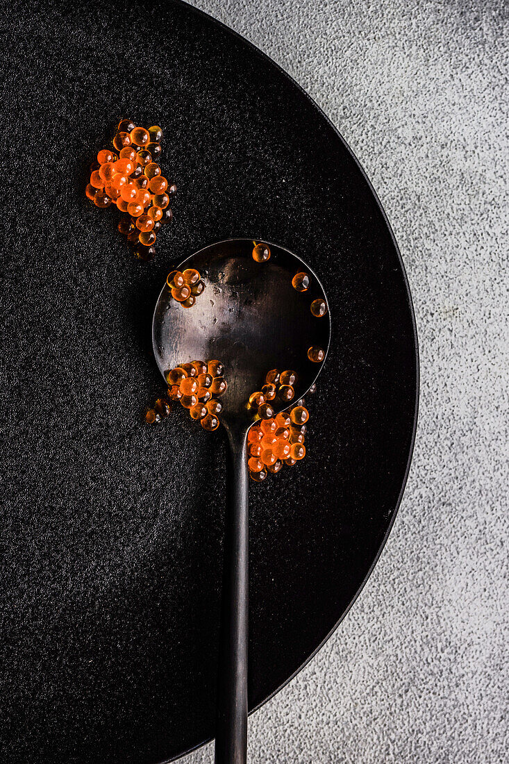 Black spoon full of red caviar on black plate and same color stone concrete table background