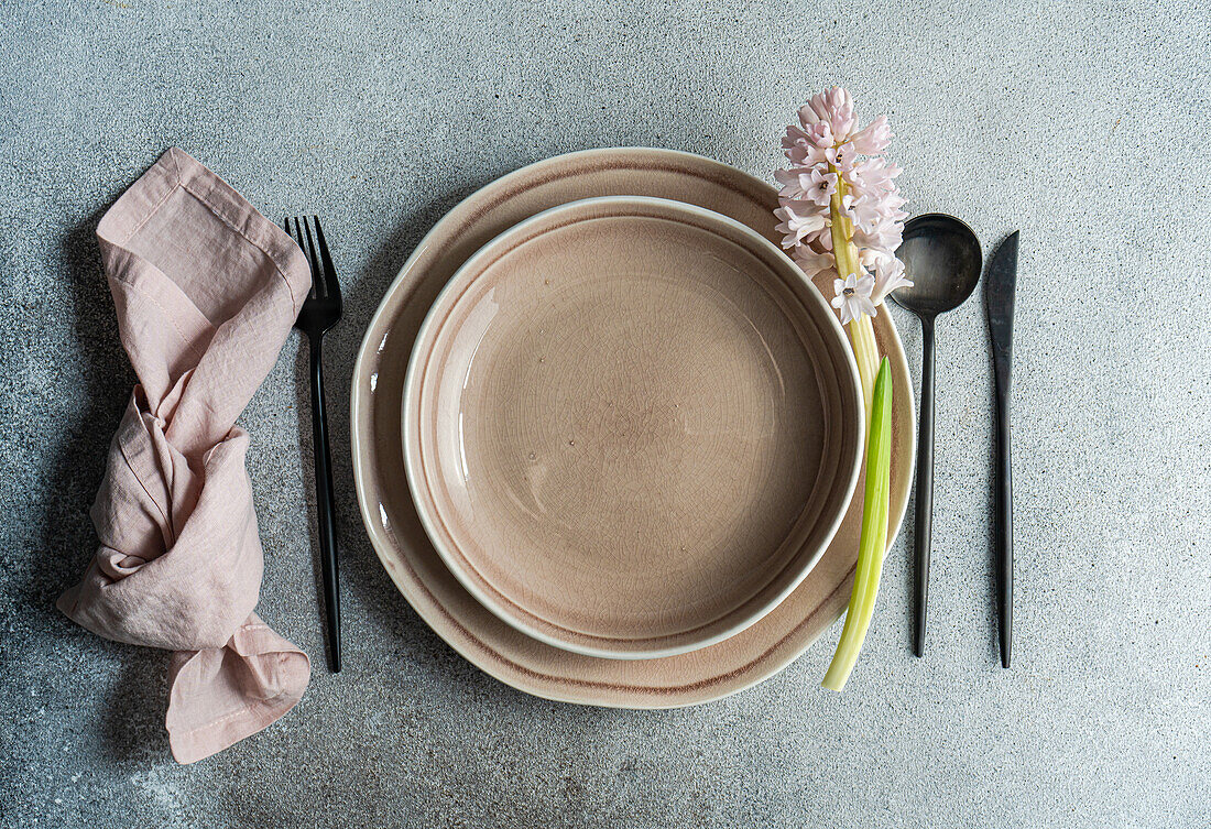 From above spring table setting with hyacinth flower near ceramic plate and cutlery on grey concrete table for festive dinner