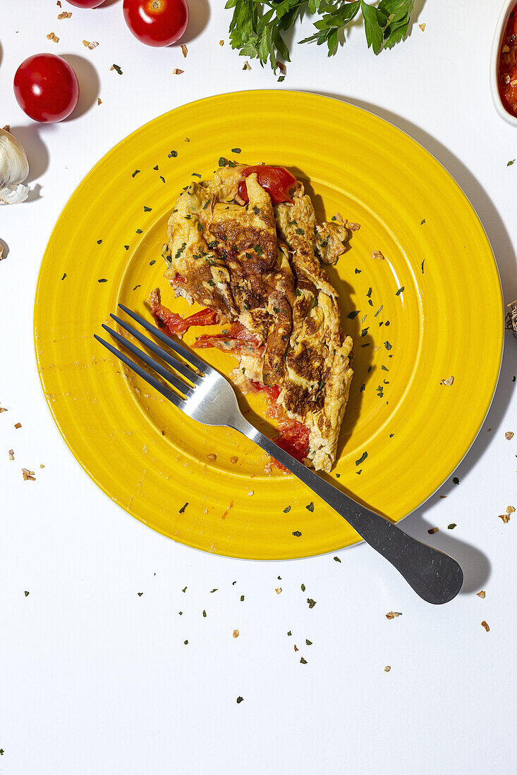 Köstliches Omelett mit gehackter Petersilie auf einem Teller mit sonnengetrockneten Tomaten auf weißem Hintergrund