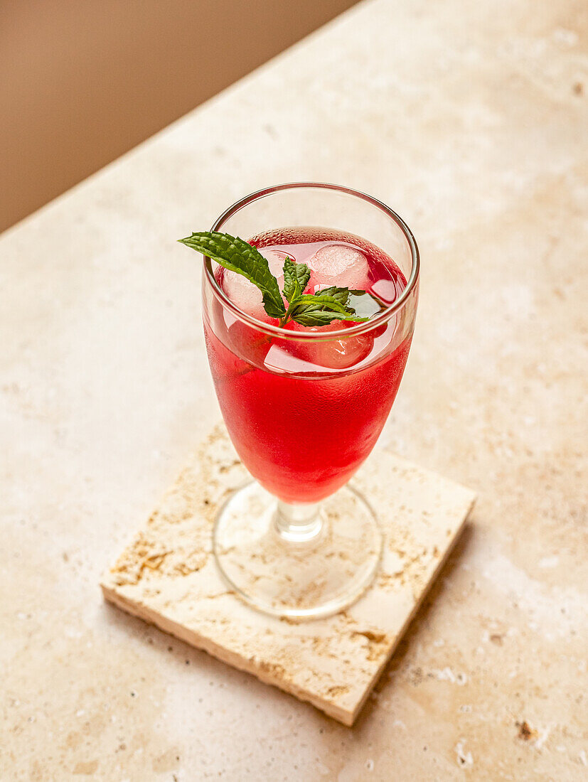 From above of tasty refreshing red beverage with ice cubes and aromatic mint leaves in glass on coaster