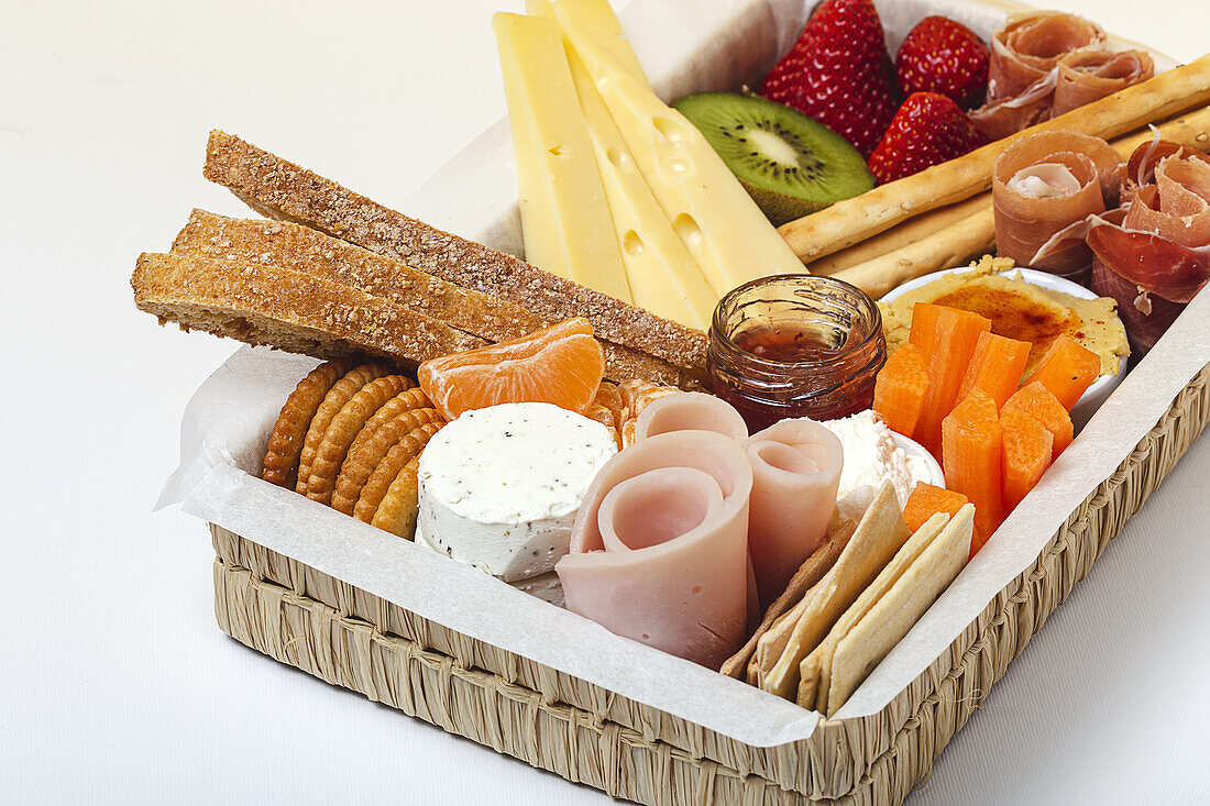 Brunch box with assorted sliced meats various types of cheese and crispbreads arranged near ripe cup kiwi sweet strawberries and peeled mandarin near jam in glass jar on colorful background