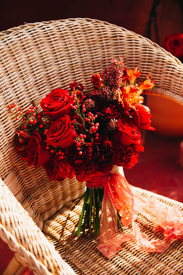 Hoher Winkel von frischen roten Blumen in einem Strauß mit dünnem Band auf einem Korbstuhl bei Sonnenschein