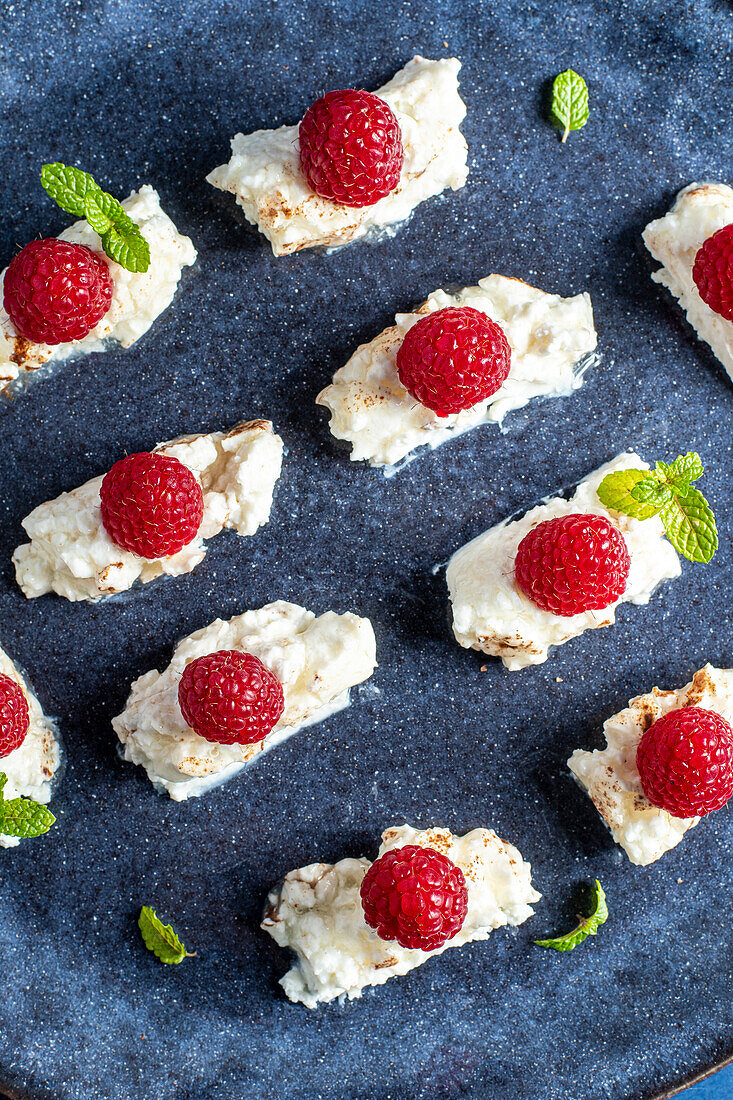 Top view of appetizing homemade dessert with cream and raspberries with mint leaves on plate placed on blue background