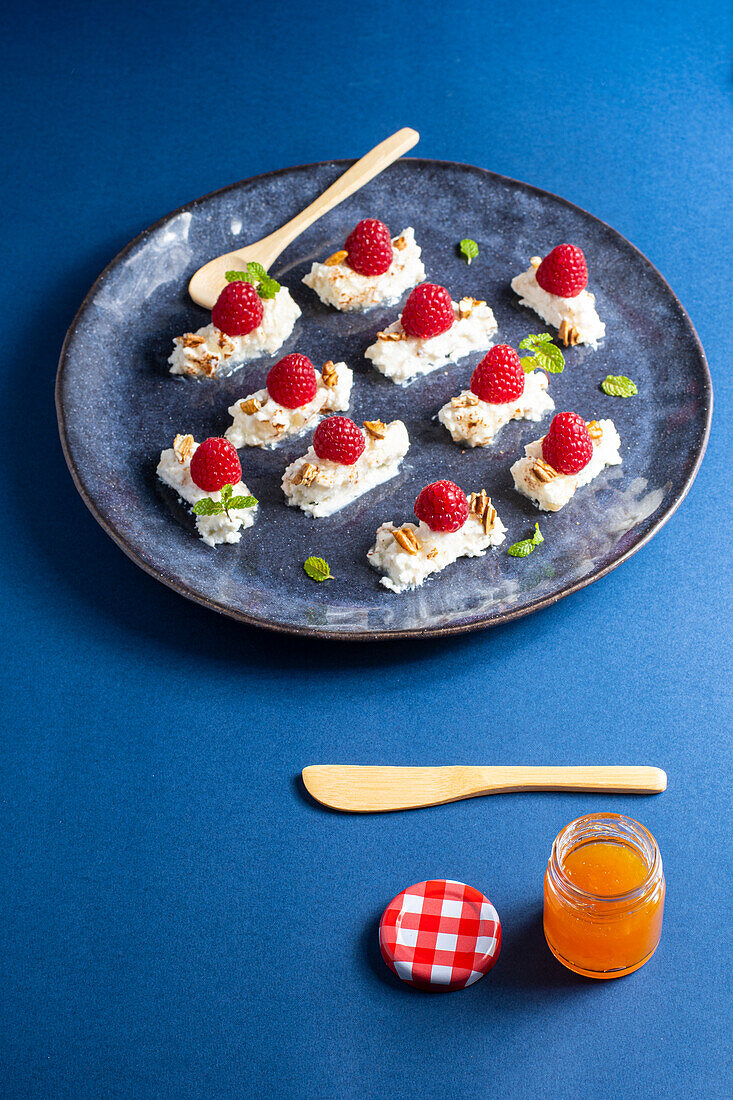 Leckeres appetitliches Dessert mit Sahne und Himbeeren, serviert mit Minzblättern und Nüssen auf einem Teller neben einem Glas Honig mit Löffel und Messer