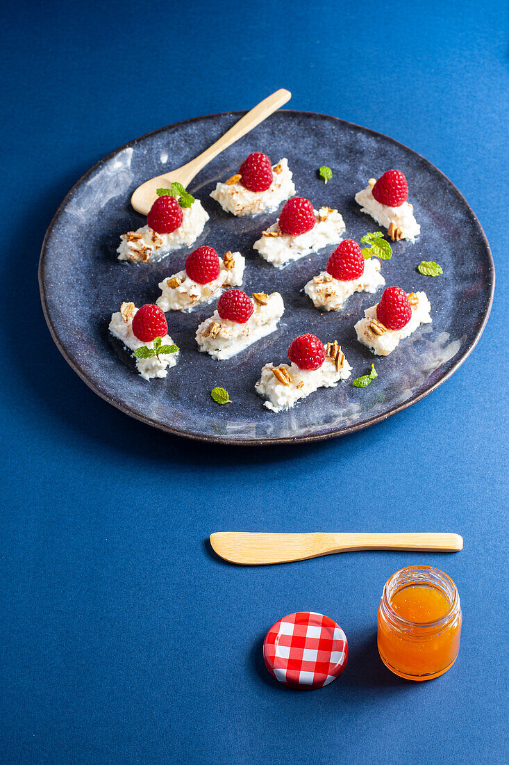 Tasty appetizing dessert with cream and raspberries served with mint leaves and nuts on plate near jar of honey with spoon and knife