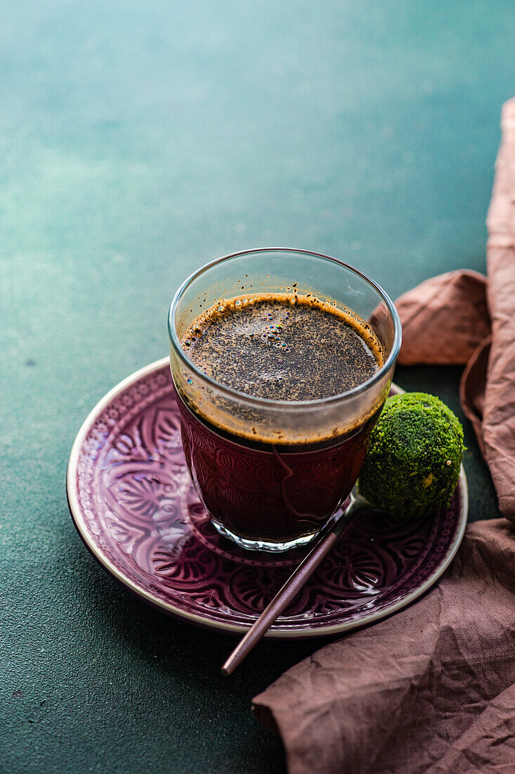 Blick von oben auf ein Glas türkischen Kaffee und traditionelle süße Pakhlava-Kugeln, serviert auf einem grünen Betontisch