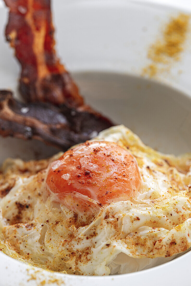 Overhead view of tasty eggs with fried bacon strips on plate