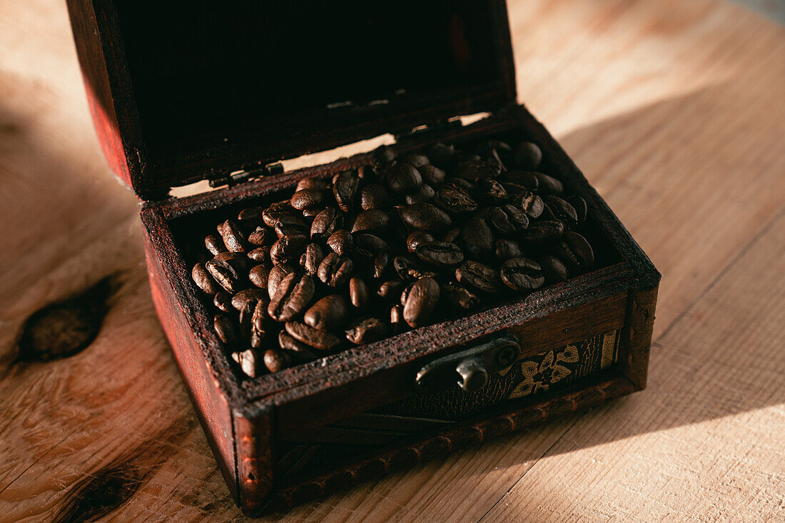 Von oben frisch geröstete aromatische Kaffeebohnen in einer Holzkiste mit antiker Kaffeemühle auf einem Tisch im Tageslicht