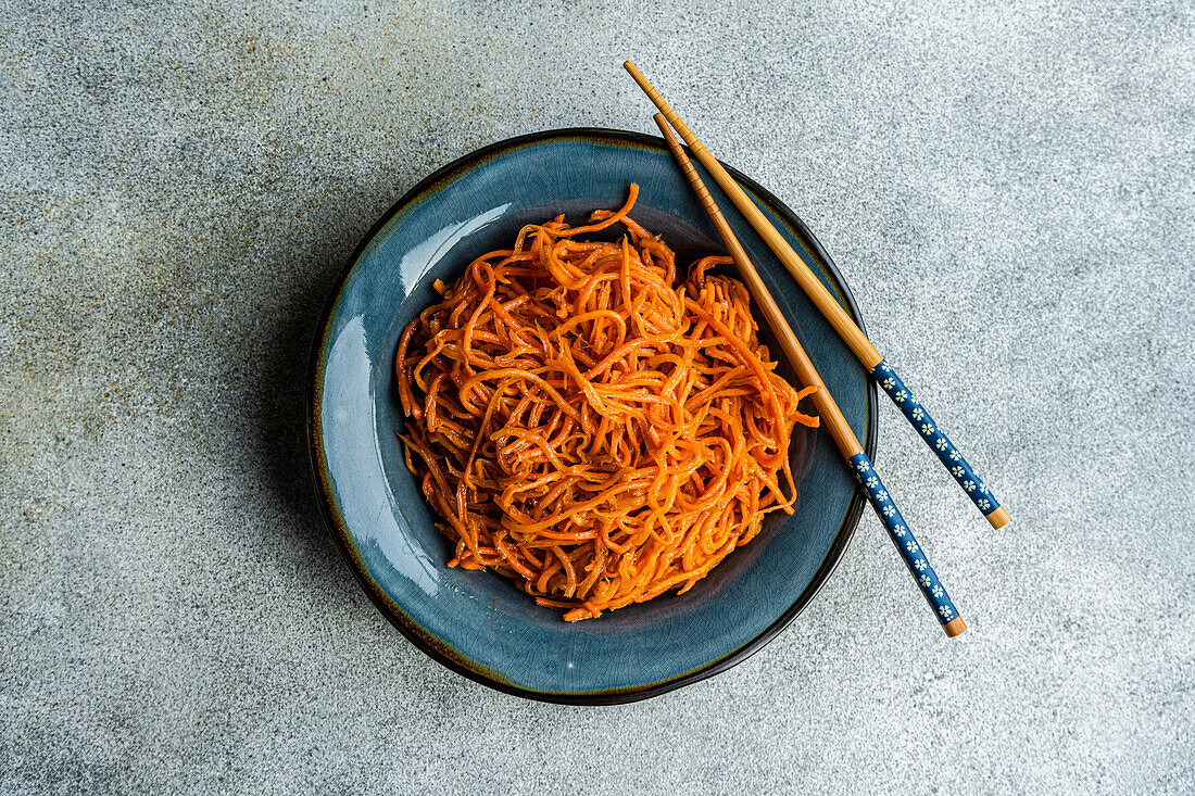 From above traditional spicy asian carrot salad served on ceramic plate and chopsticks on concrete background