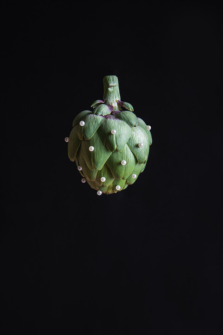 Frische Knospe einer grünen Artischockenpflanze mit kleinen Perlen, die auf einen schwarzen Hintergrund fallen