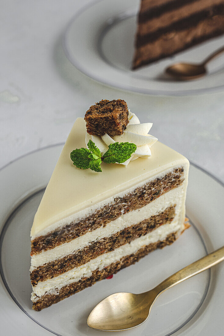 Piece of yummy sweet chocolate cake decorated with whipped cream served on ceramic plate with golden spoon on white tablecloth