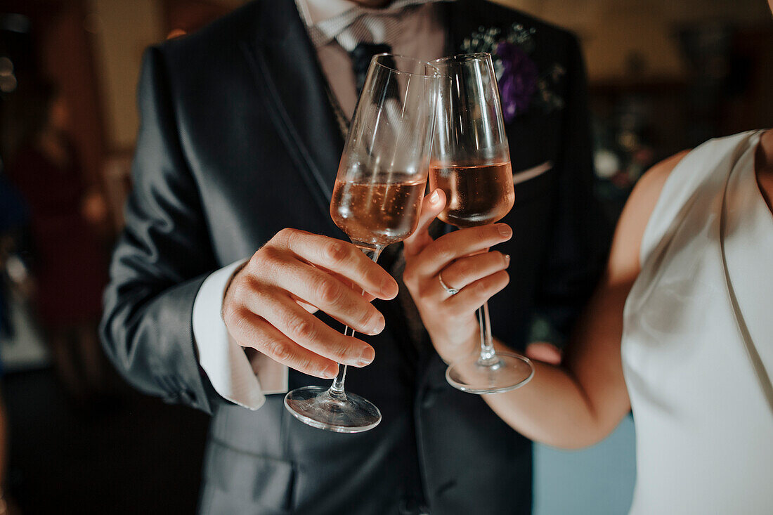 Anonyme Braut und Bräutigam in eleganter Hochzeitskleidung stoßen bei einer Feier mit Sekt an