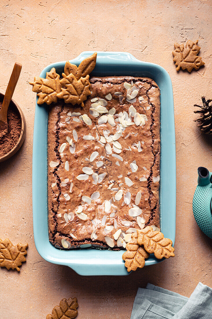 Draufsicht auf leckeren gebackenen Brownie mit Mandelblättchen im Backblech mit Keksen auf dem Tisch mit Kakaopulver