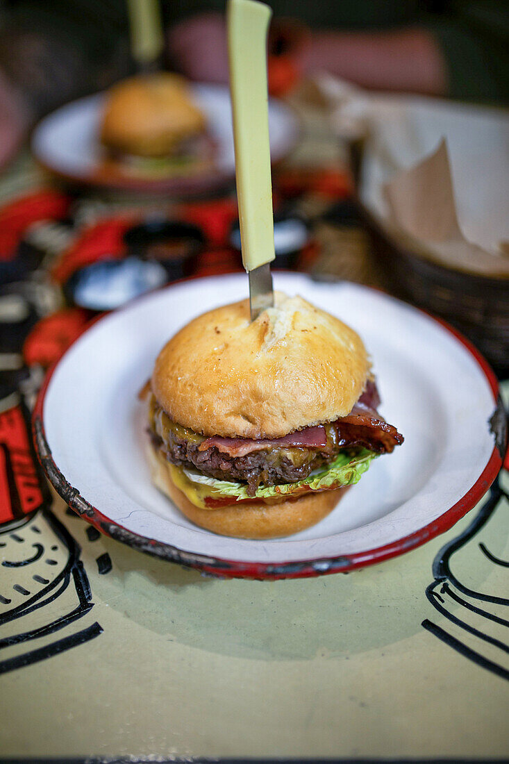 High angle of delicious burger with meat bacon and lettuce served on plate with knife in restaurant