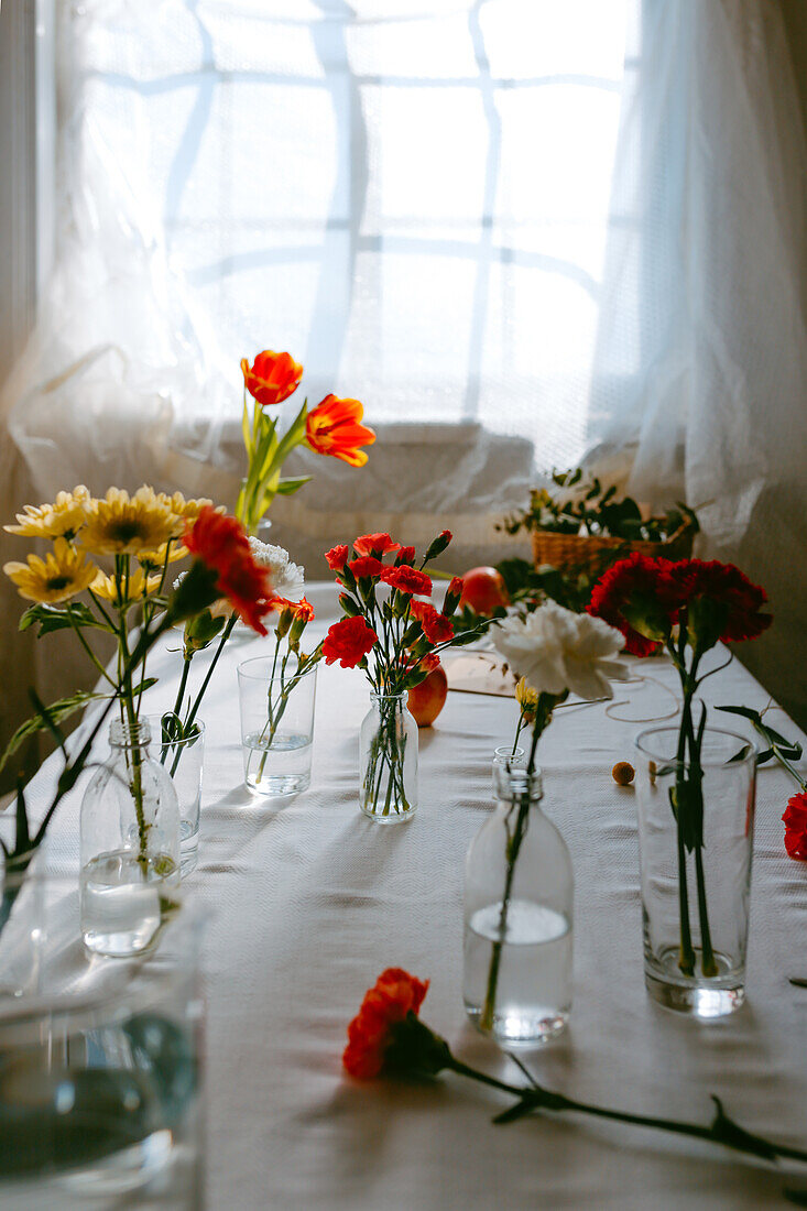 Gläser mit frischen Tulpen und Nelken in Wasser auf dem Tisch für Blumensträuße