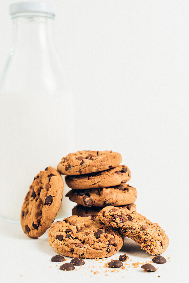 Heap of sweet crunchy cookies with chocolate drops placed on table with empty bottle in light room on white background