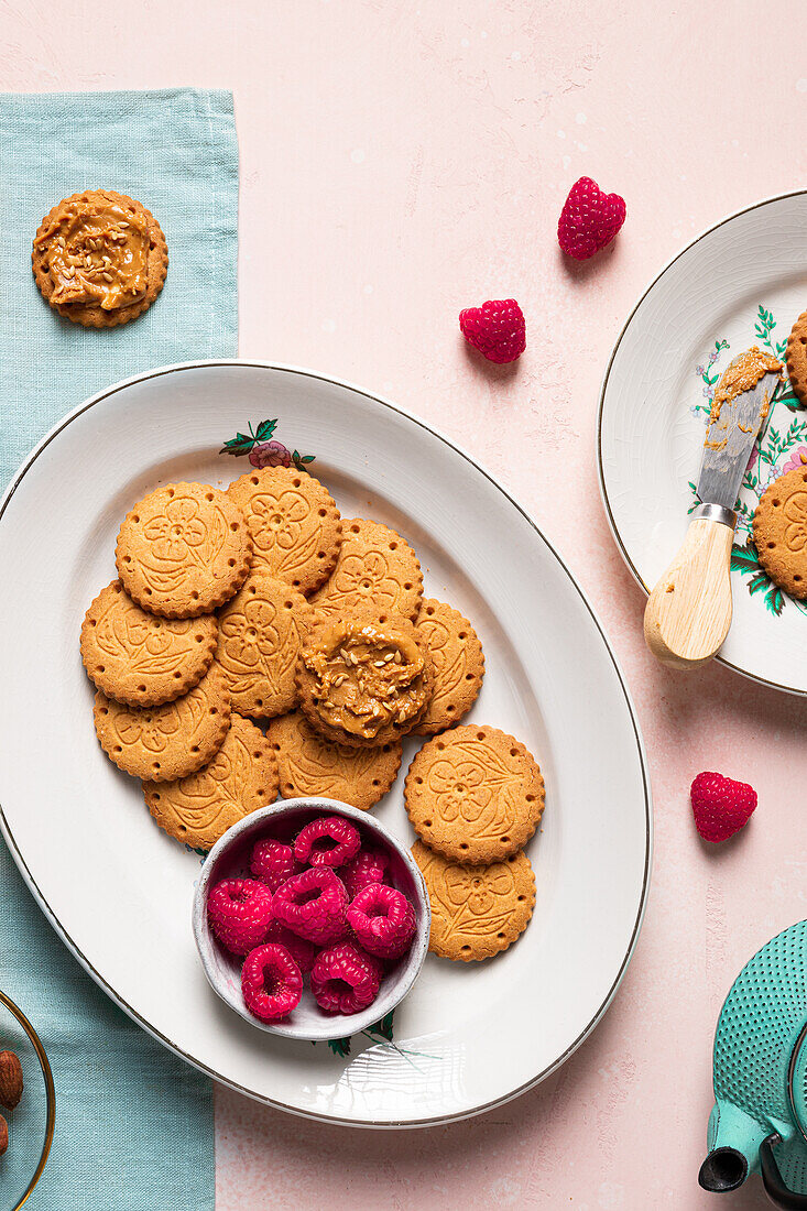 Top view of plates with delicious crispy homemade cookies and fresh raspberries served on table with teapot bowl of seeds