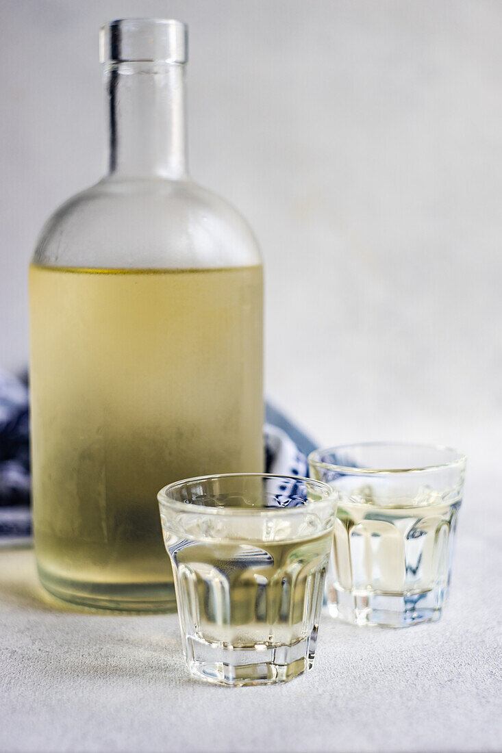 Georgian grape chacha drink in the bottle and glasses on grey concrete table with white Supra tablecloth