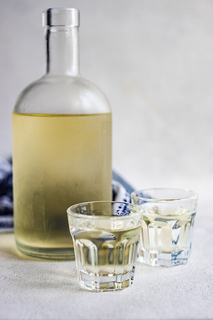 Georgisches Traubentschacha-Getränk in der Flasche und Gläser auf grauem Betontisch mit weißer Supra-Tischdecke