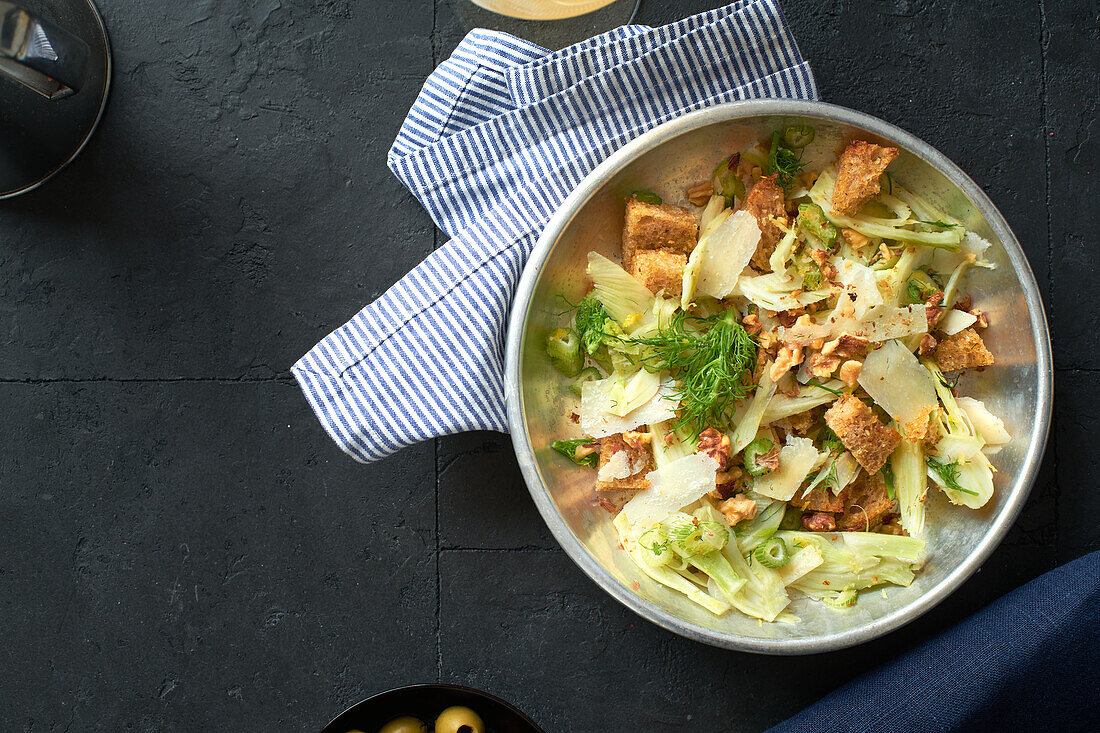 Fenchelsalat von oben mit Parmesankäse, Walnüssen und Croutons auf grauem Hintergrund