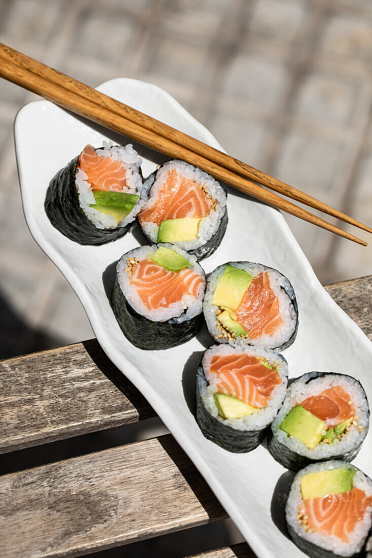 Von oben schmackhafte japanische Sushi-Rollen mit norwegischem Lachs Futomaki auf gepflastertem Gehweg mit Stäbchen auf einer sonnigen Straße in der Stadt platziert