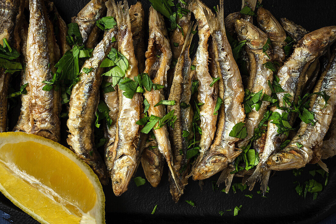 Overhead view of appetizing Fried anchovies with chopped parsley and fresh lemon slice with juicy flesh