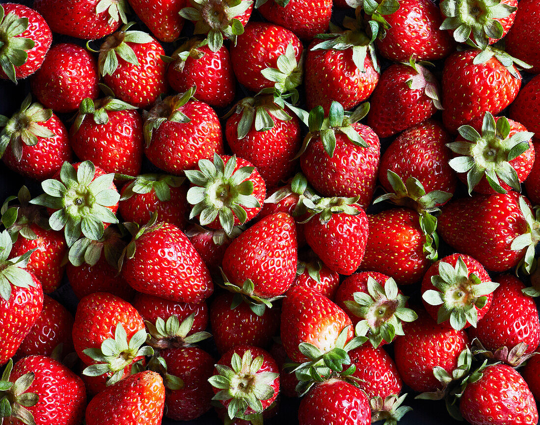 From above closeup of fresh ripe strawberries with green leaves as background representing concept of healthy food