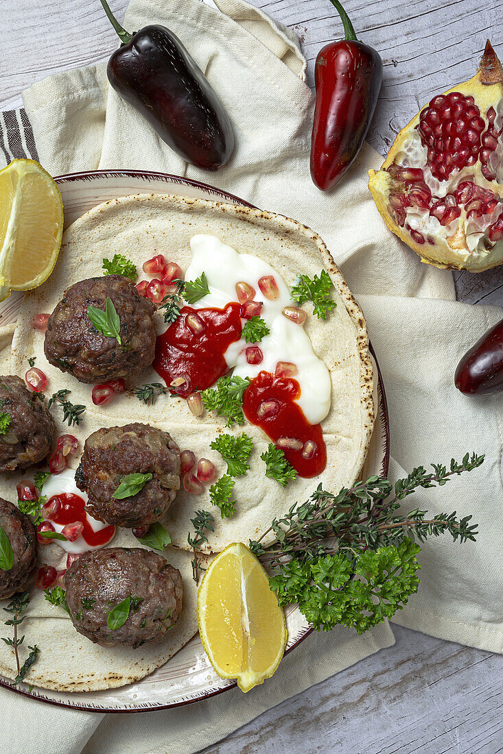 Traditional homemade beef and lamb meatballs with arabic bread, tomato sauce, pomegranate and aromatic herbs. Halal food