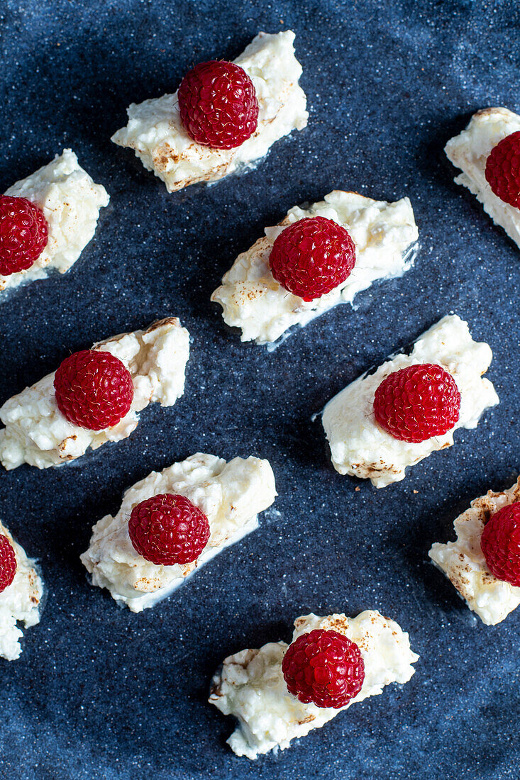 Top view of appetizing homemade dessert with cream and raspberries on plate placed on blue background