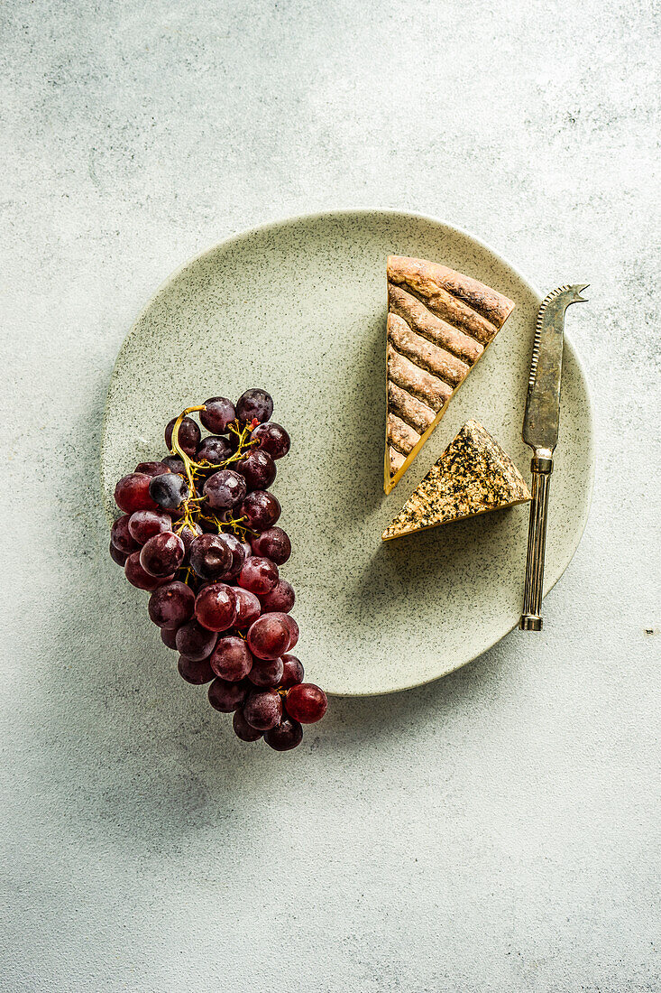 From above stone plate with variation of cheese and raw tasty grape on concrete table