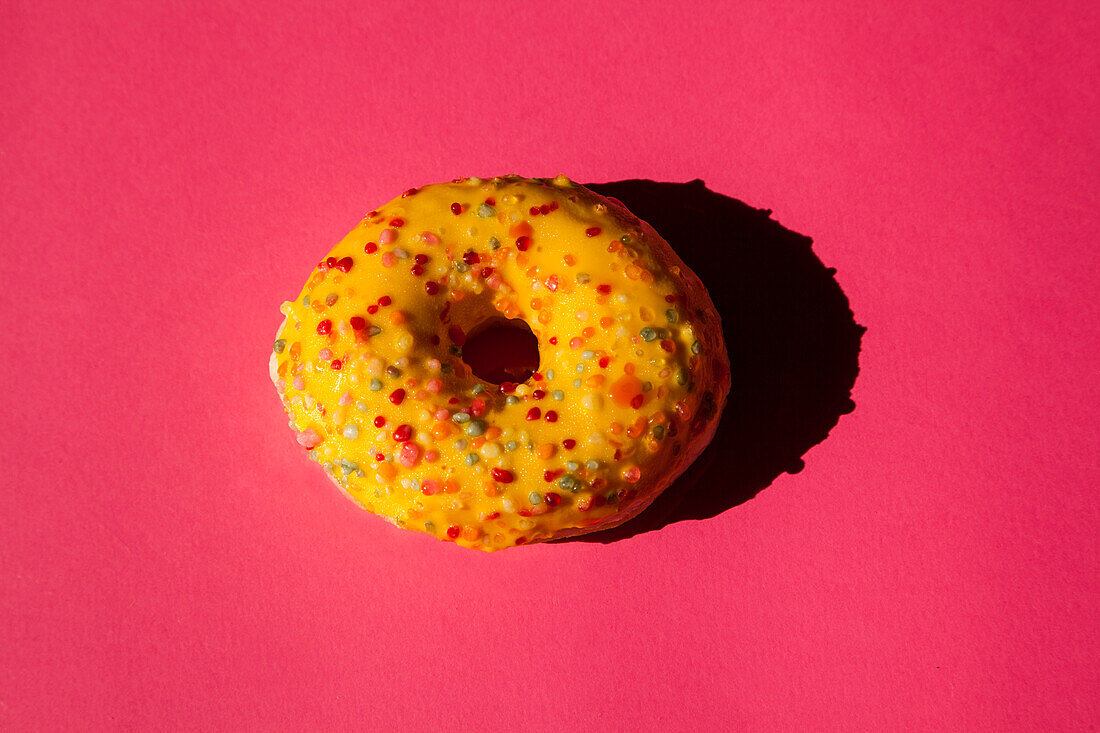 Top view of one donuts coated with a yellow sugar with colored balls on pink background