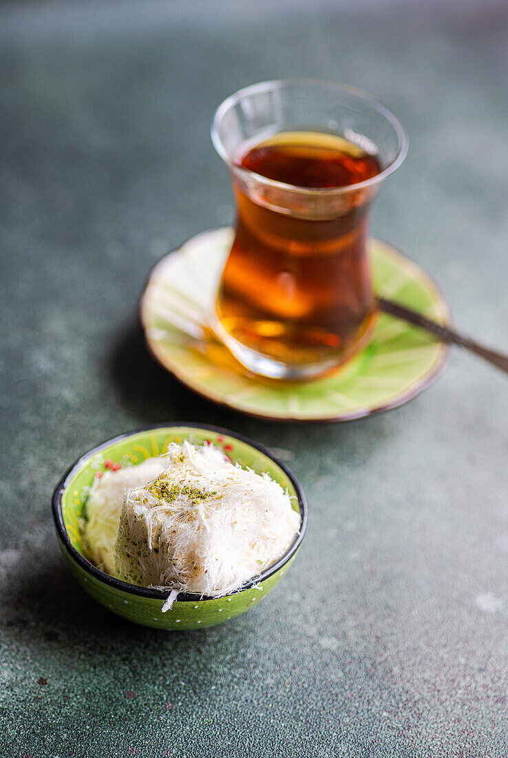 Türkische Zuckerwattebonbons und schwarzer Tee im Glas serviert auf Betonhintergrund