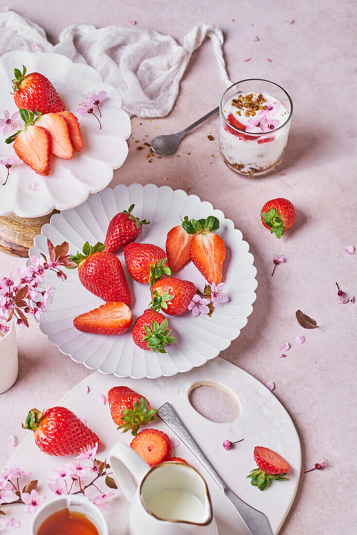 Blick von oben auf ein Glas köstlichen Joghurts mit Müsli auf einem Tisch neben Tellern mit frischen reifen Erdbeeren, die auf einem Tisch in der Küche serviert werden