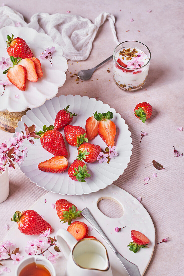 From above of glass of delicious yogurt with granola placed on table near plates of fresh ripe strawberries served on table in kitchen