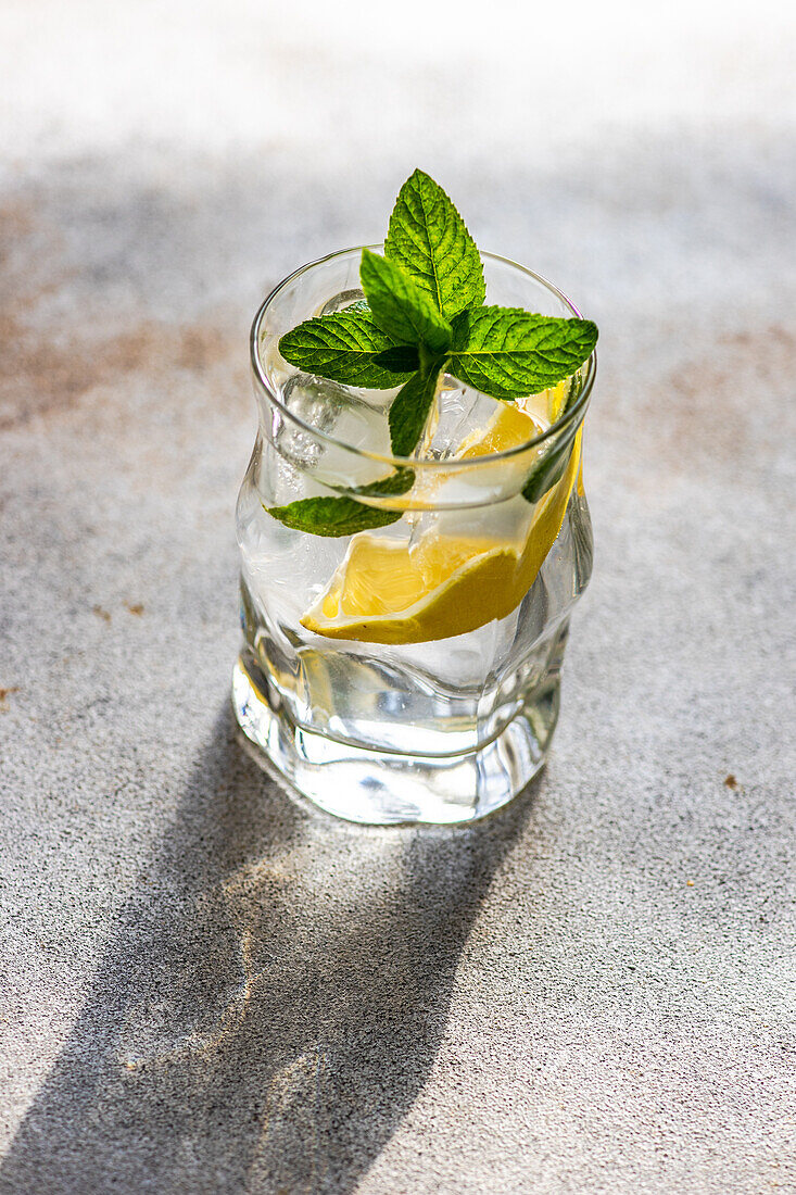 Glass of lemon water with mint on concrete background in sunny day with shadows
