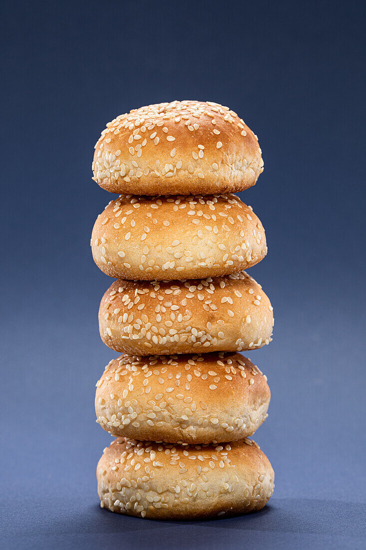Bunch of yummy whole burger buns with sesame stacked together on blue background