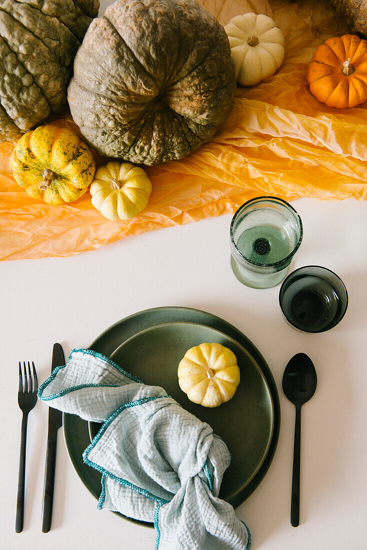 Top view of glasses and plate with napkin served on table decorated with assorted pumpkins during Halloween celebration