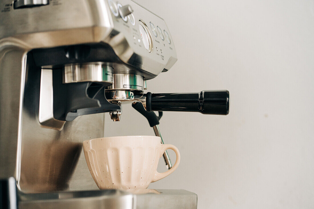 Ceramic cup on stainless steel coffee maker with portafilter in kitchen on white background