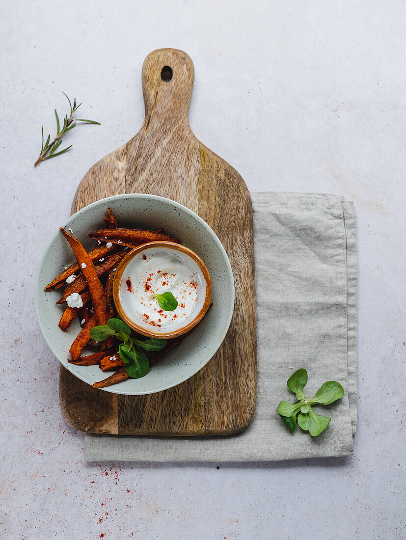 High angle of delicious sweet potato fries with sour cream and herbs served on table