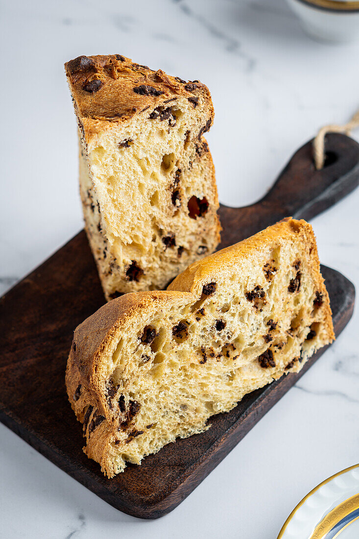 From above rustic traditional Christmas panettone cake with raisins sliced on wooden board among luxurious breakfast tableware