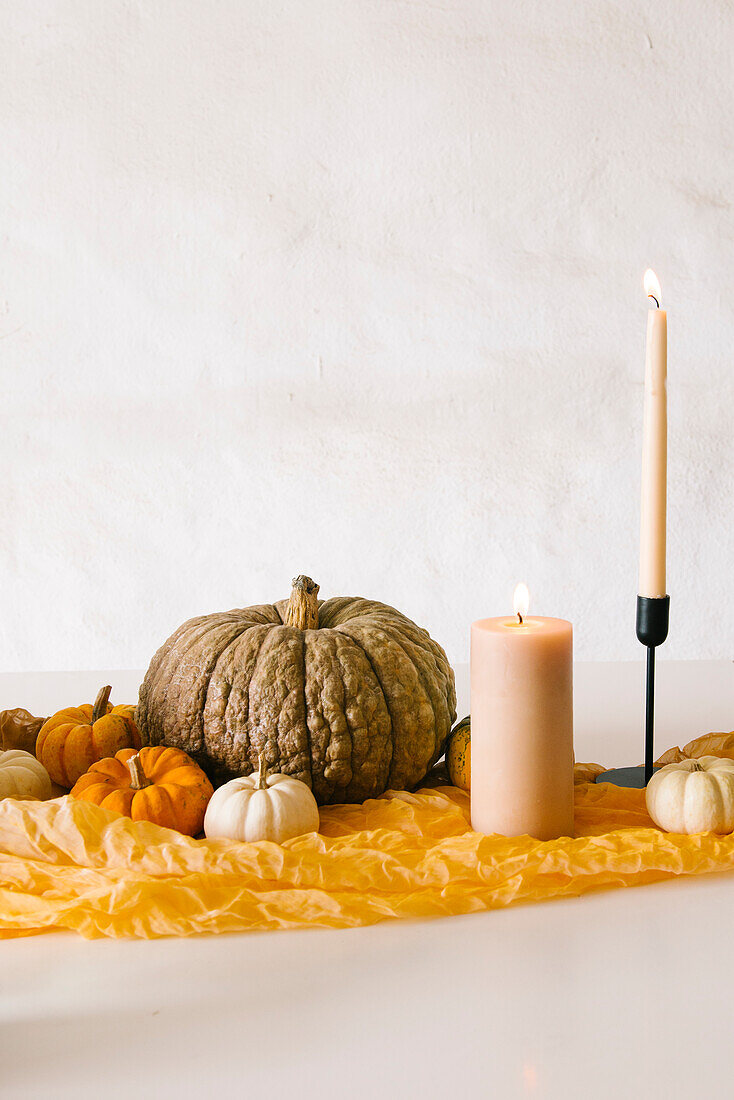 Brennende Kerzen in Stöcken und verschiedene Kürbisse auf einem weißen Tisch während einer Halloweenfeier